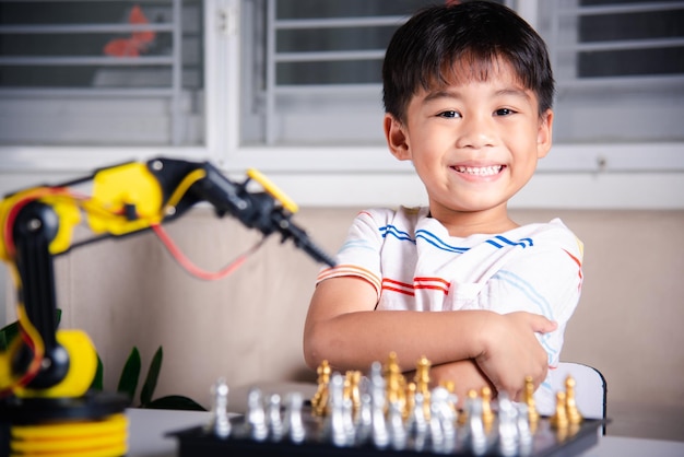 El niño asiático está jugando al ajedrez con el brazo de la máquina robot