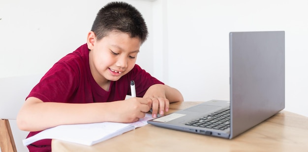 Niño asiático estudiando en línea en computadora portátil con cara sonriente y feliz en casa educación en línea