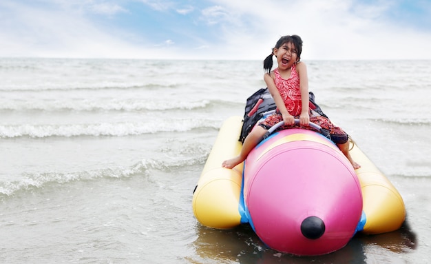 Niño asiático feliz en un barco de plástico en la playa en verano