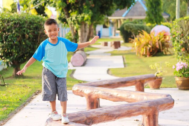 Niño asiático feliz calentar su cuerpo antes de correr y hacer ejercicio. Caminaba sobre una barra de madera en el patio de recreo.