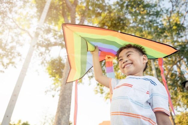 Niño asiático feliz con una cometa corriendo para volar en el parque al atardecer de verano al aire libre