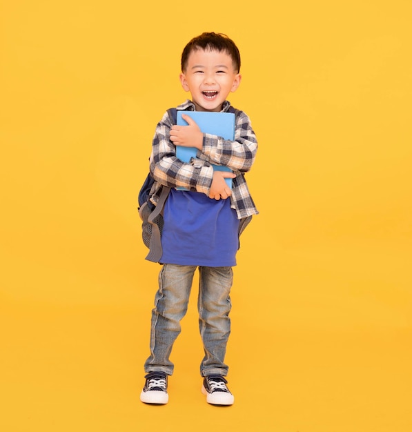 Niño asiático feliz sosteniendo o abrazando un gran libro sobre fondo amarillo