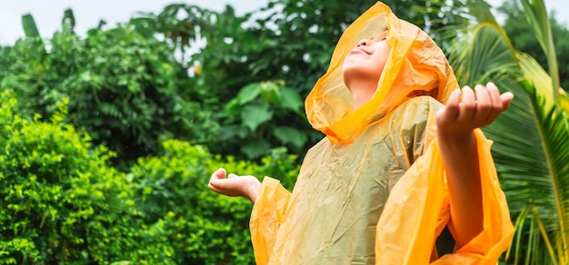 Niño asiático con impermeable naranja está feliz y divirtiéndose bajo la lluvia en un día lluvioso
