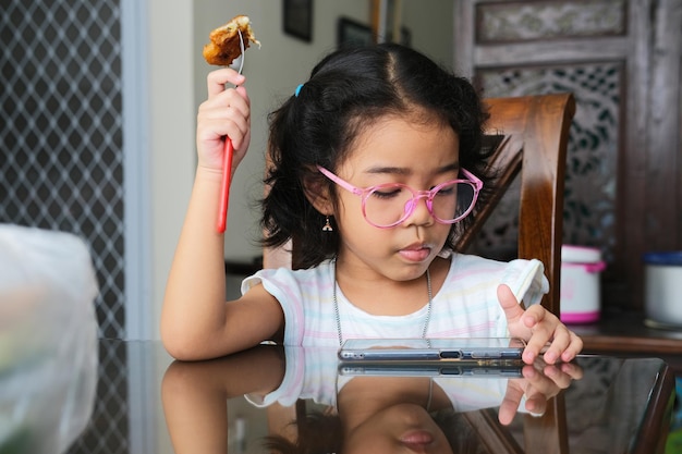 Niño asiático jugando con su teléfono móvil mientras come bocadillos