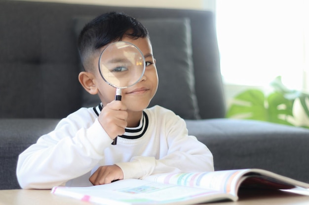 Niño asiático leyendo los libros en el escritorio con una lupa