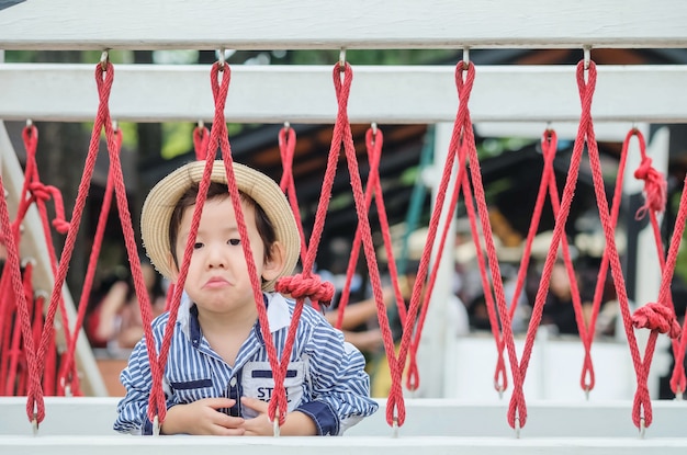 Niño asiático lindo del primer con la cara agujereada en un puente en fondo del patio
