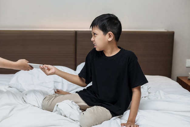 Niño asiático llorando cuando su teléfono inteligente es tomado por mamá