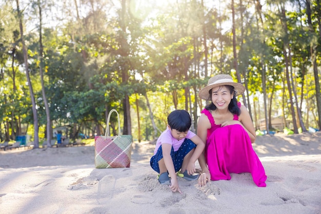 Niño asiático y mujer mamá relajándose en la playa tropical disfrutan de la libertad y el aire fresco con sombrero y ropa con estilo Feliz turista sonriente en los trópicos en vacaciones de viaje