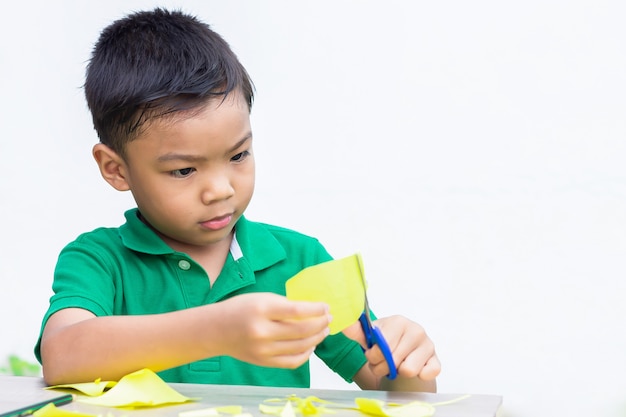 Niño asiático niño práctica para cortar papel de color con las tijeras en la mesa de madera.