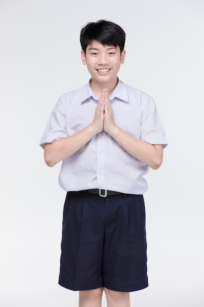 Foto niño asiático niño en uniforme de estudiante, actuando sawaddee significa hola.