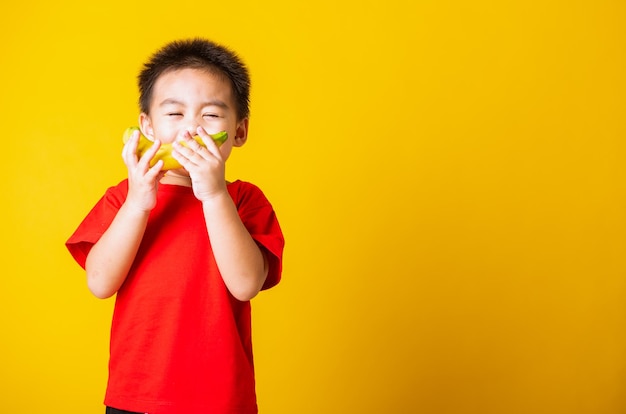 Niño asiático o niño lindo niño pequeño sonrisa atractiva con camiseta roja jugando tiene fruta de plátano