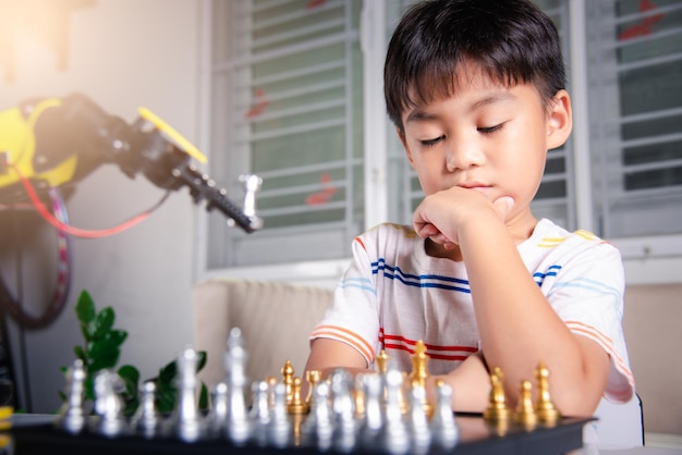 Niño asiático pensando y esperando brazo robot jugando al ajedrez