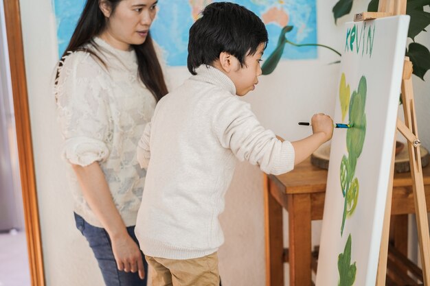 Niño asiático pintando sobre lienzo durante la clase de arte en casa - Centrarse en la cara del niño