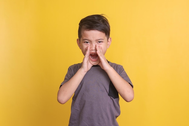 Foto un niño asiático pone la mano alrededor de los labios y grita al frente de la cámara haciendo un gesto de anuncio