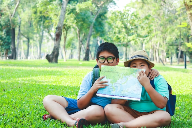 Un niño asiático de primaria sentado en el césped del jardín con un mapa para estudiar la información.