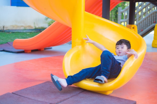 Niño asiático que juega la diapositiva en el patio bajo la luz del sol en verano