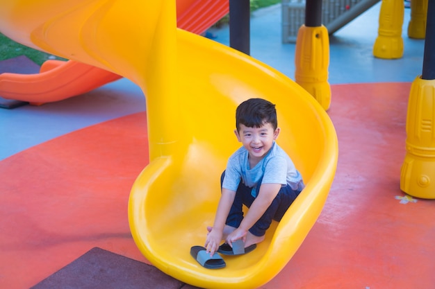 Niño asiático que juega la diapositiva en el patio bajo la luz del sol en verano