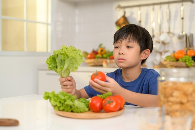 Niño asiático que se siente aburrido infeliz por comer verduras concepto de atención médica