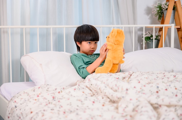 Niño asiático solo en casa y jugar con muñeca. Hijo con juguete como amigo. Chico solitario infeliz.