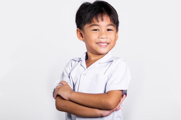 Un niño asiático sonríe feliz usando un uniforme tailandés de estudiante con pantalones rojos de pie con los brazos cruzados