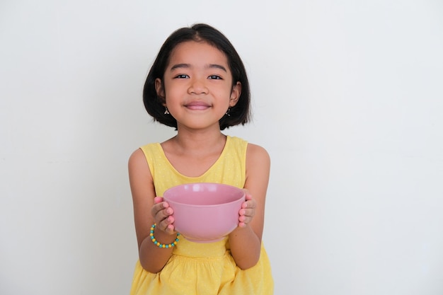 Niño asiático sonriendo a la cámara mientras sostiene un plato de cena vacío