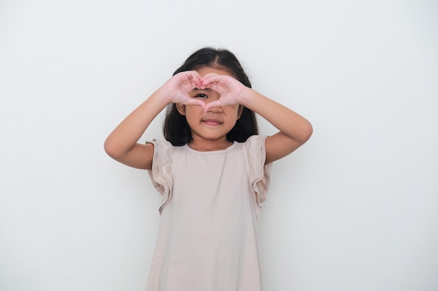 Niño asiático sonriendo mientras mira a escondidas de la mano en forma de corazón Concepto de amor