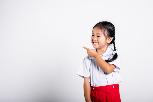 Niño asiático sonriente feliz vistiendo estudiante uniforme tailandés falda roja sigue señalando con el dedo en el espacio de la copia