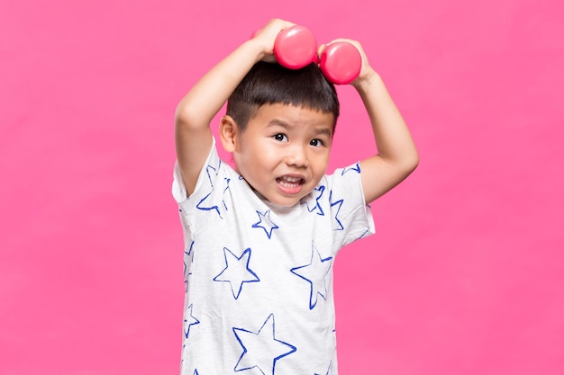 Niño asiático sosteniendo una manivela sobre un fondo rosado