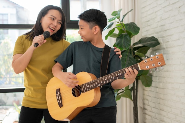 El niño asiático tocando la guitarra y la madre cantan una canción y se abrazan, se sienten apreciados y alentados.