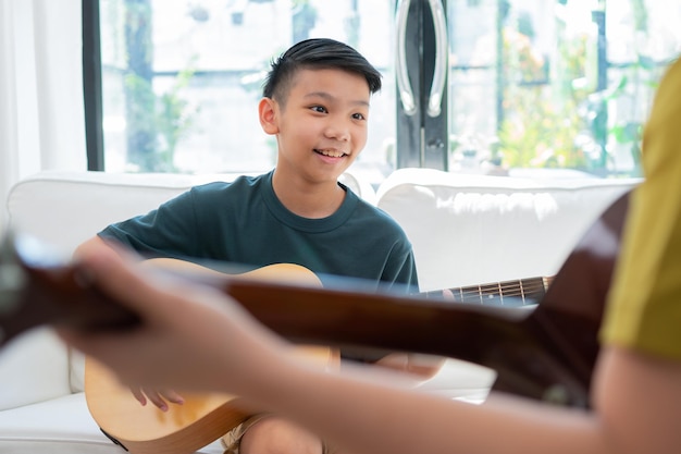 Niño asiático tocando la guitarra con su padre en la sala de estar por enseñarle a su hijo a tocar la guitarra