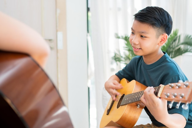 Niño asiático tocando la guitarra con su padre en la sala de estar por enseñarle a su hijo a tocar la guitarra