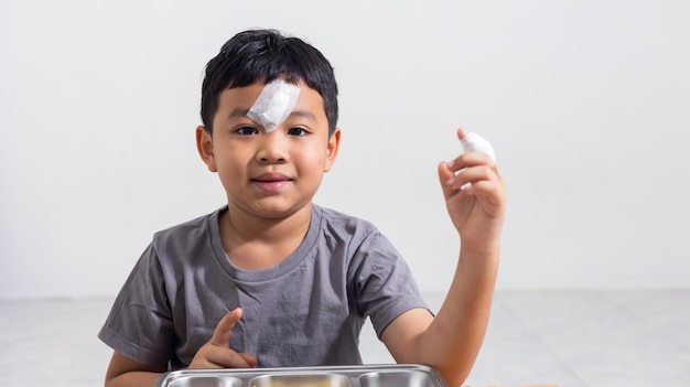 Foto un niño asiático está triste tenía heridas en la cara y los dedos un niño asiático resultó herido en un accidente mientras jugaba aislado en un fondo blanco seguro de vida