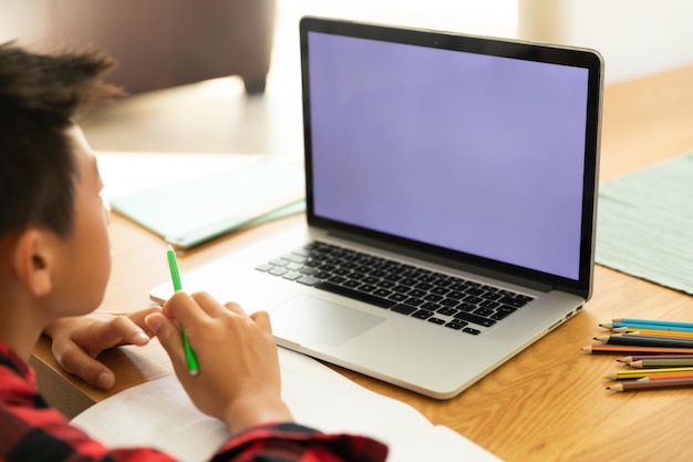 Niño asiático usando una computadora portátil con pantalla en blanco en casa. estilo de vida doméstico y educación en línea durante el concepto de pandemia covid 19.