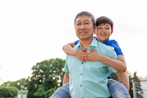 Niño asiático volando hacia adelante en la espalda de su padre en verano jubilado coreano jugando con su hijo