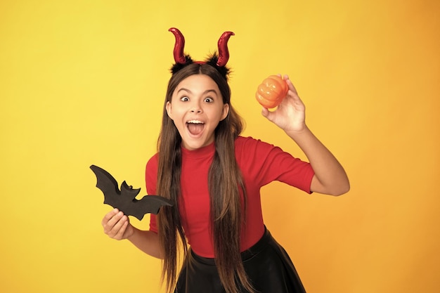 Foto niño asombrado con calabaza y murciélago con cuernos de diablo sobre fondo amarillo feliz halloween