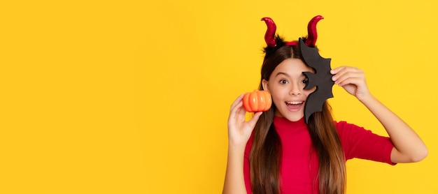 Niño asombrado en cuernos de diablillo sostiene calabaza y murciélago sobre fondo amarillo alegría Halloween niño niña