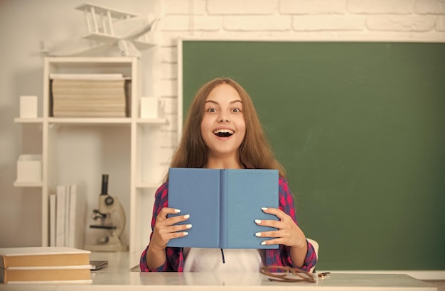 Niño asombrado hacer la tarea con el libro adolescente estudiante educación moderna escuela secundaria