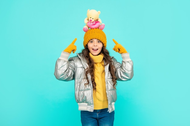 Foto niño asombrado con sombrero y chaqueta de globo señala con el dedo el juguete en la tienda de juguetes de fondo azul