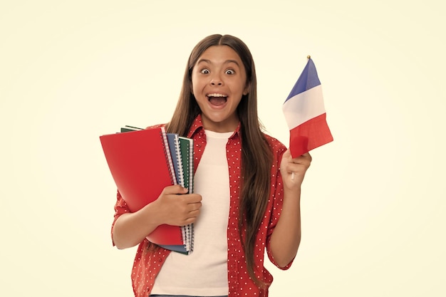 Niño asombrado sostiene la bandera francesa y el cuaderno escolar para estudiar aislado en blanco estudiar en el extranjero