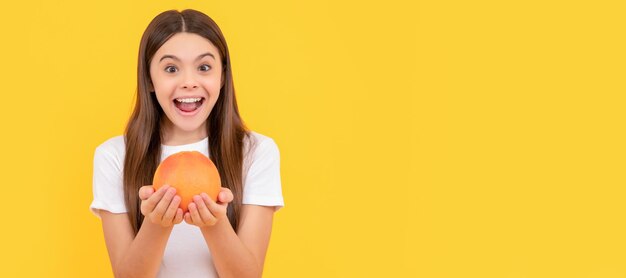 Niño asombrado sostiene pomelo sobre fondo amarillo salud Retrato de niña niño con cartel horizontal naranja pomelo Encabezado de banner con espacio de copia