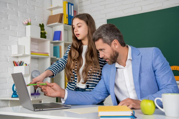 Un niño asombrado con un tutor en el aula usa una computadora portátil