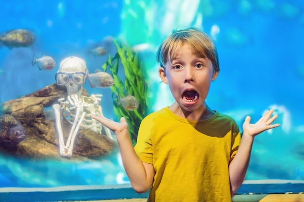 El niño se asustó Esqueleto y piraña en un acuario.