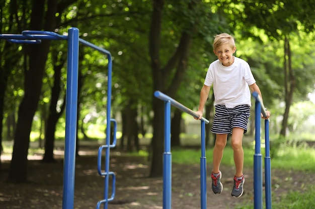 Niño atleta en el parque en el travesaño para flexiones hizo una mueca e intenta realizar los ejercicios