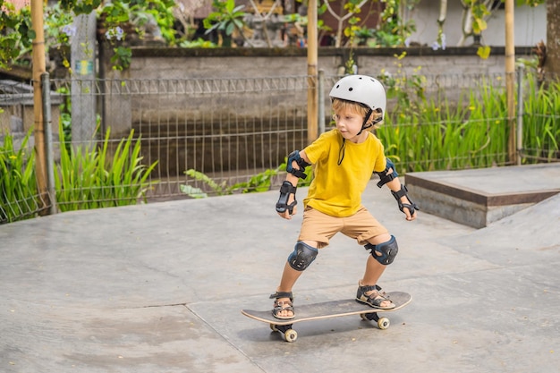 Foto niño atlético con casco y rodilleras aprende a andar en monopatín en un parque de patinaje deportes educativos para niños