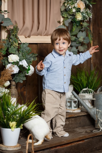 Niño atractivo jugando con el conejito de Pascua en un pasto verde. Decoración rústica Foto de estudio sobre un fondo de madera