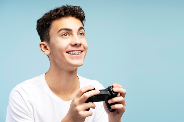 Un niño atractivo sonriente con aparatos ortopédicos sostiene usando la consola jugando a un videojuego mirando hacia otro lado