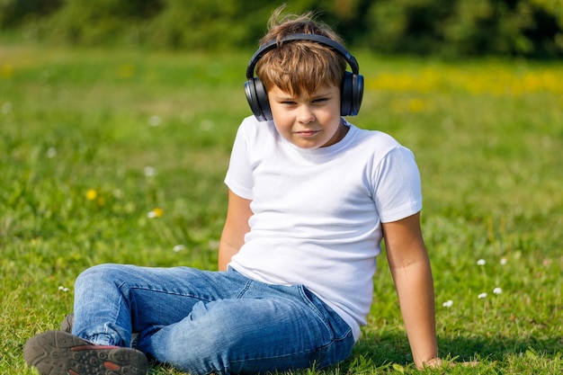 Niño con auriculares escuchando música mientras está sentado en el césped del parque