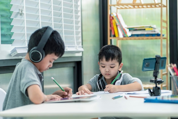 Niño con auriculares está usando una tableta y se comunica en Internet en casa. educación en el hogar, aprendizaje a distancia, niño asiático tomando una clase en línea y feliz por la cuarentena de la escuela en el hogar.