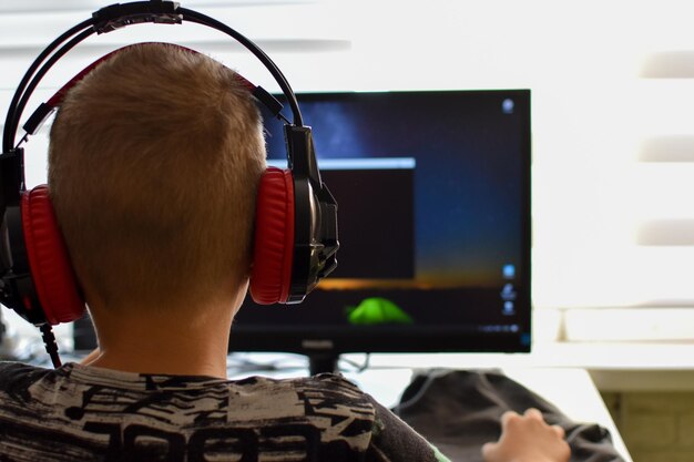 Un niño con auriculares se sienta en una computadora jugando un juego. adicción a los dispositivos de juego de los niños