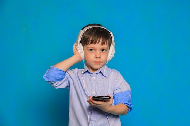 Un niño con auriculares sobre un fondo azul Auriculares para niños Daño de auriculares para el niño Audiolibros útiles para niños Un artículo sobre ocio infantil Música